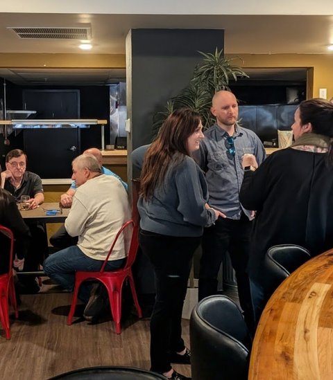 Members standing and chatting beside a curved wooden bar
