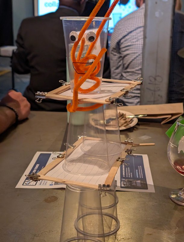 A googly-eyed pipe cleaner creature perched on top of a team's cup tower