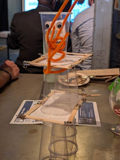 A googly-eyed pipe cleaner creature perched on a guest-built cup tower at Next Level Networking