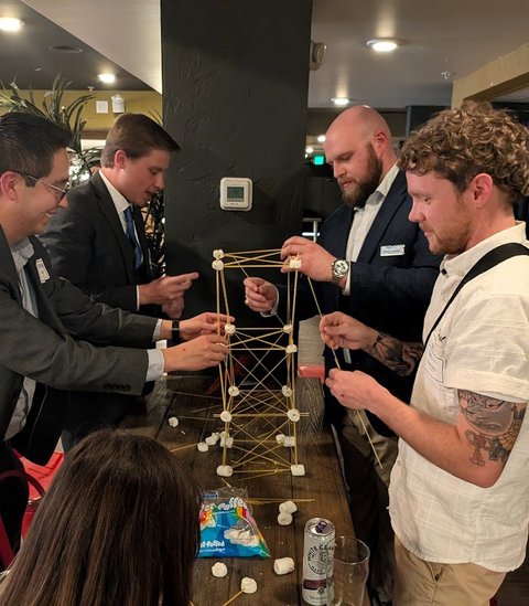 Members in suits building a spaghetti tower together