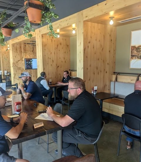 Members talking at tables in a light, plant-filled restaurant